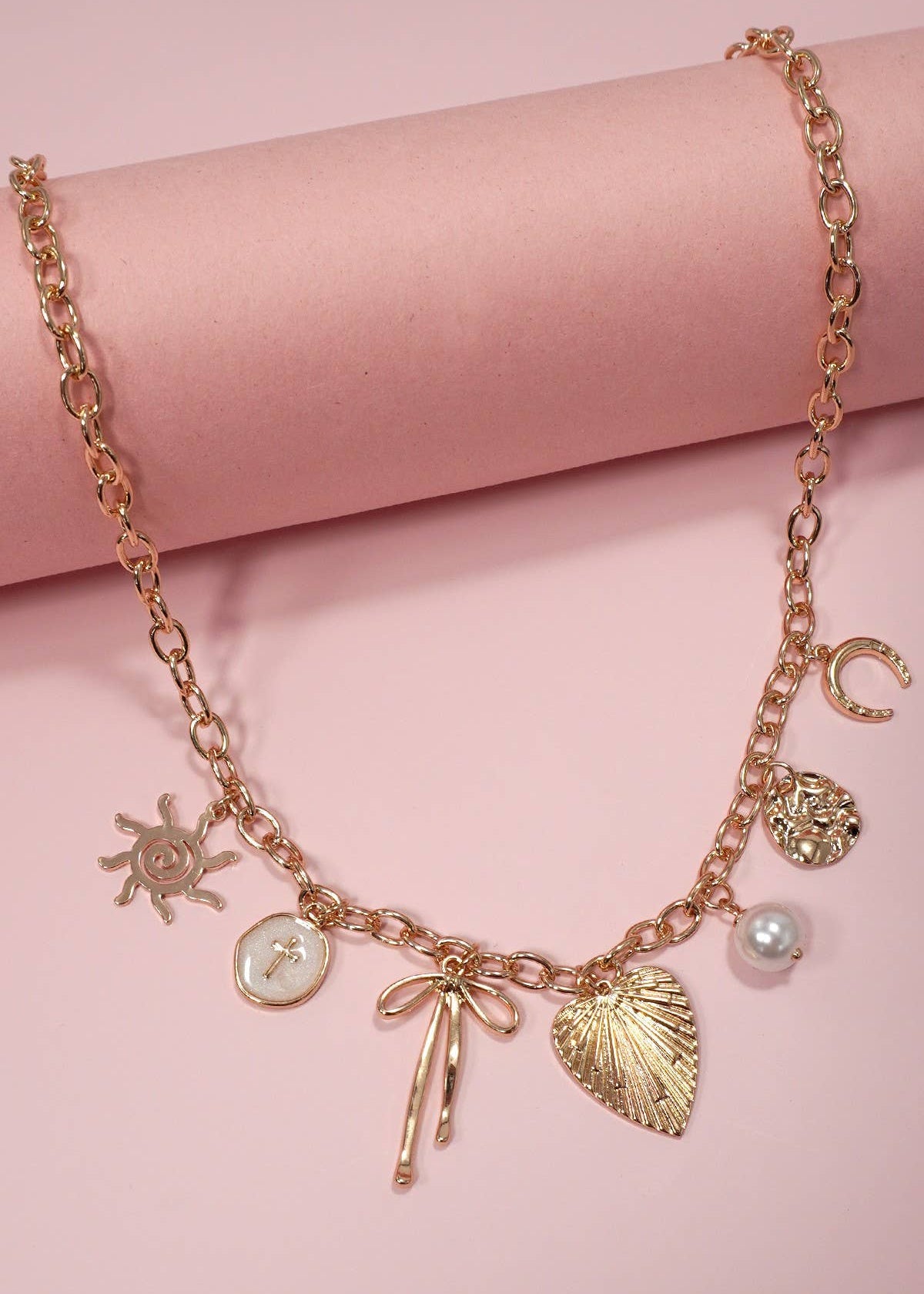 Gold statement charm necklace with a sun, cross, bow, heart, pearl and horseshoe accent. 