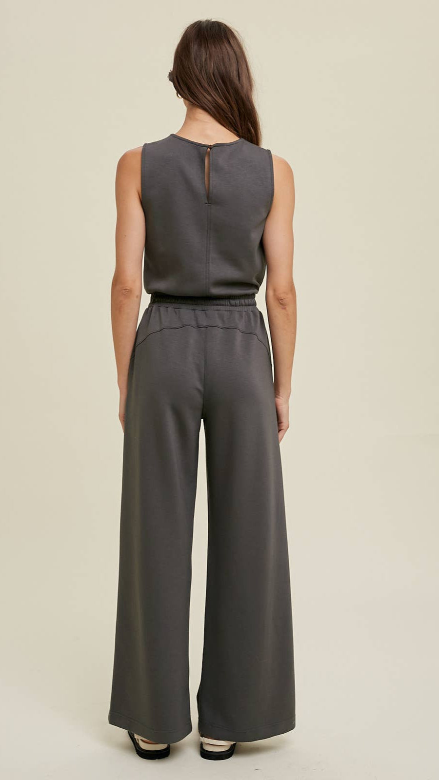 Wide-leg dark sleeveless grey jumpsuit with an elastic waistband, side pockets, and back keyhole detail.