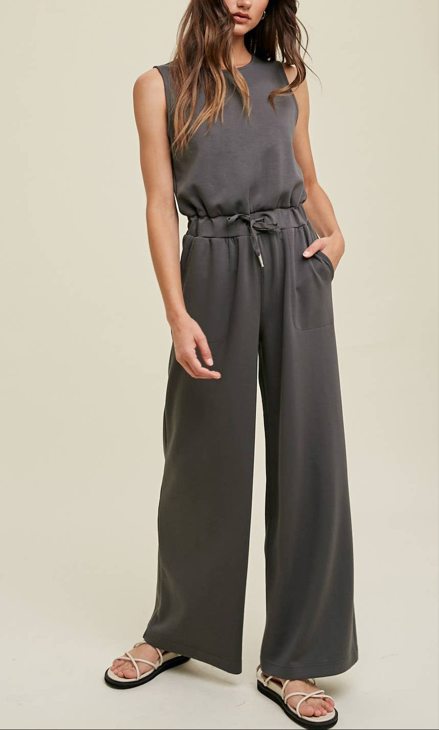 Wide-leg dark sleeveless grey jumpsuit with an elastic waistband, side pockets, and back keyhole detail.