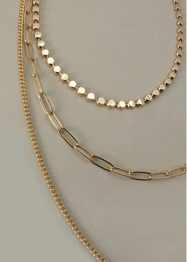 Gold multi-layer chain necklace with three distinct chains and adjustable length.