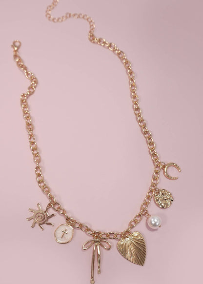 Gold statement charm necklace with a sun, cross, bow, heart, pearl and horseshoe accent. 