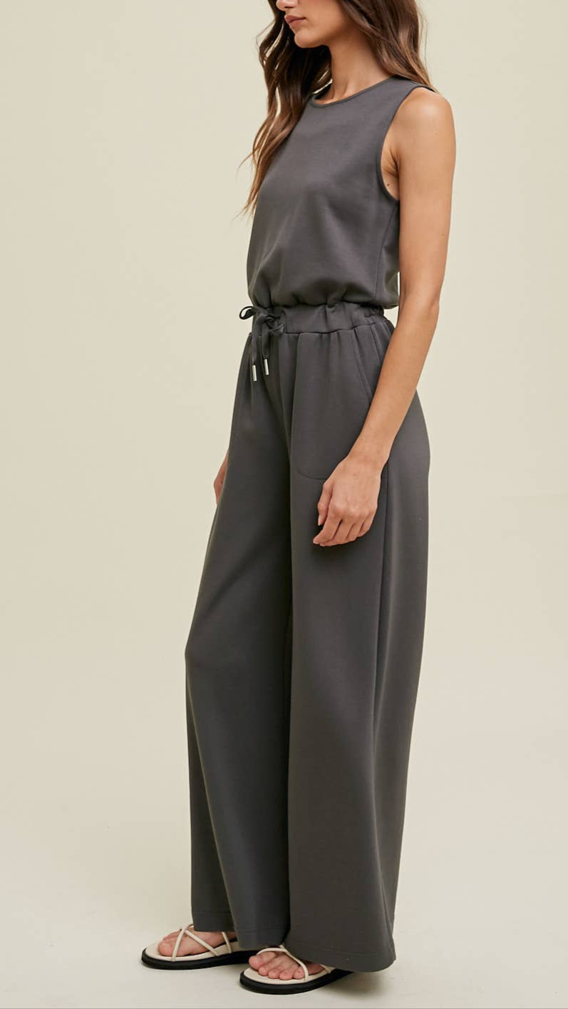 Wide-leg dark sleeveless grey jumpsuit with an elastic waistband, side pockets, and back keyhole detail.