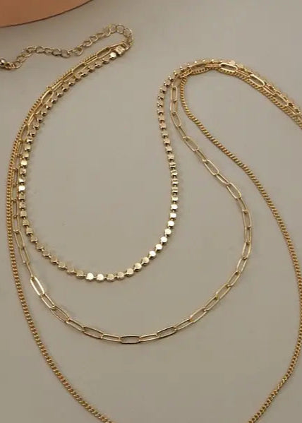 Gold multi-layer chain necklace with three distinct chains and adjustable length.