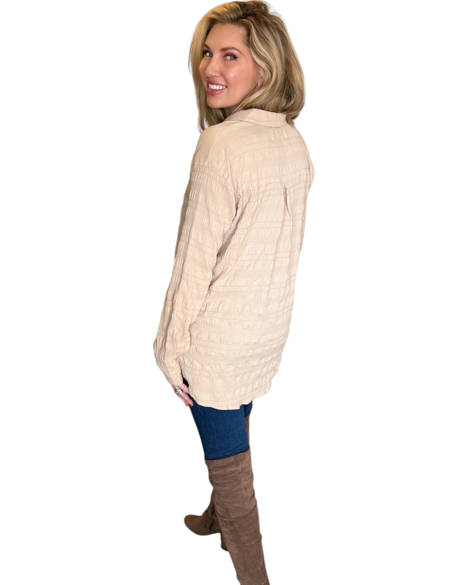 Blonde woman smiling while wearing the Almond Button Down Shirt paired with blue jeans. The shirt features a textured fabric, long sleeves, and a relaxed fit with a curved hem. 