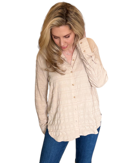 Blonde woman smiling while wearing the Almond Button Down Shirt paired with blue jeans. The shirt features a textured fabric, long sleeves, and a relaxed fit with a curved hem. 