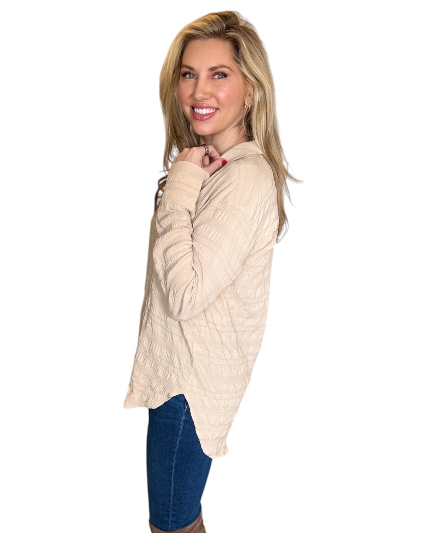 Blonde woman smiling while wearing the Almond Button Down Shirt paired with blue jeans. The shirt features a textured fabric, long sleeves, and a relaxed fit with a curved hem. 