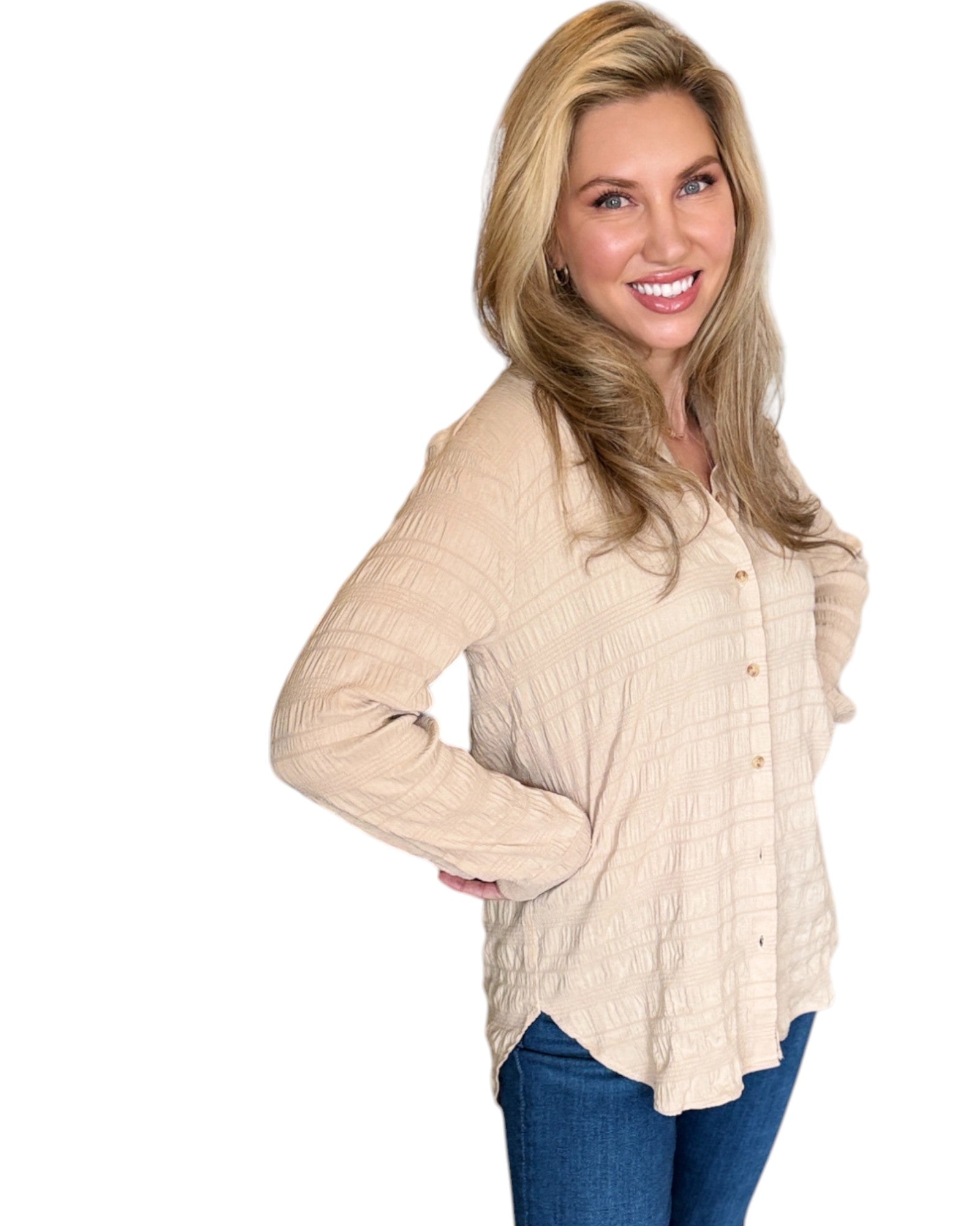 Blonde woman smiling while wearing the Almond Button Down Shirt paired with blue jeans. The shirt features a textured fabric, long sleeves, and a relaxed fit with a curved hem. 