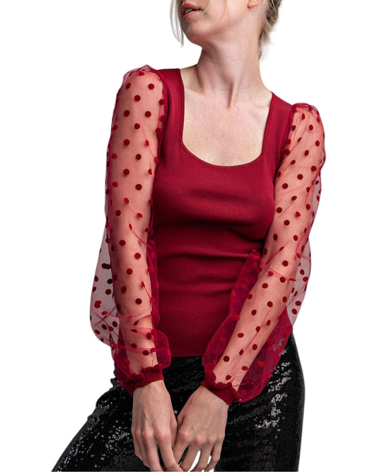 Woman wearing a merlot colored top with long, sheer sleeves with velvet polka dots. 