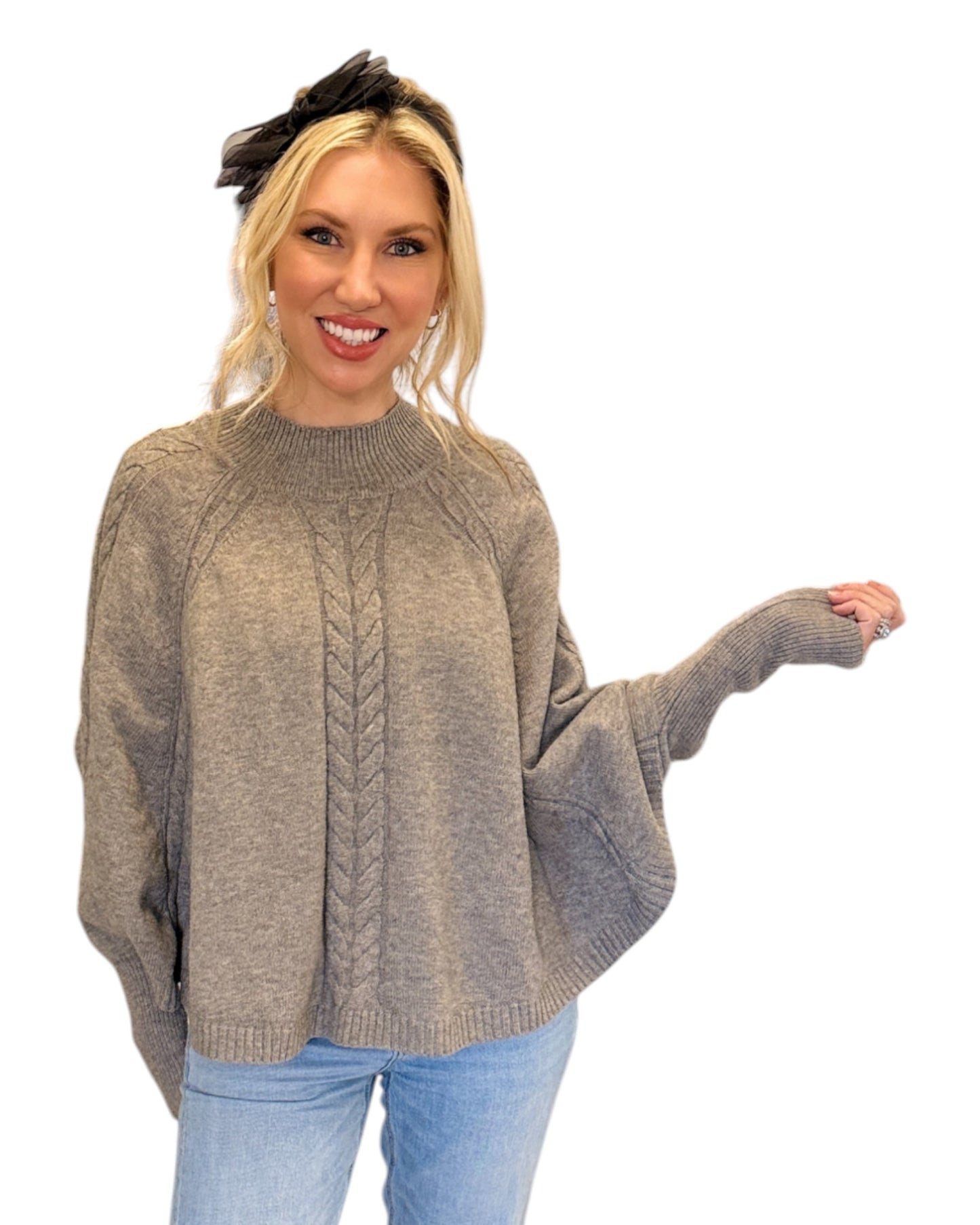 Woman wearing jeans and a Heather Grey/Taupe Cable Knit Mock Neck Poncho with a relaxed silhouette, cable knit design, and fitted sleeve hem, perfect for cozy layering.