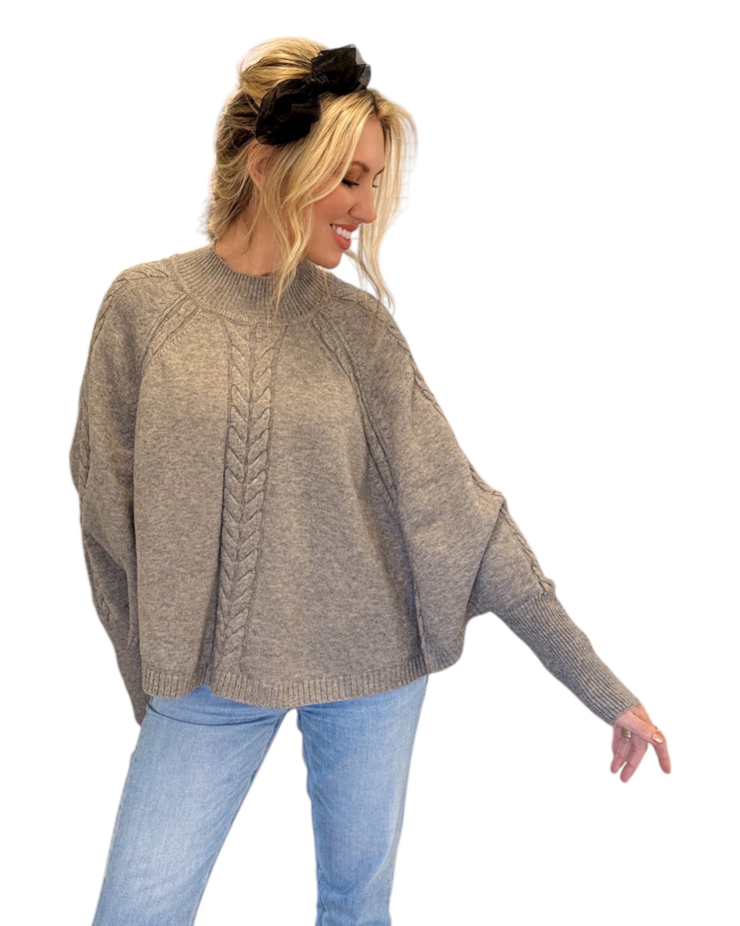 Woman wearing jeans and a Heather Grey/Taupe Cable Knit Mock Neck Poncho with a relaxed silhouette, cable knit design, and fitted sleeve hem, perfect for cozy layering.