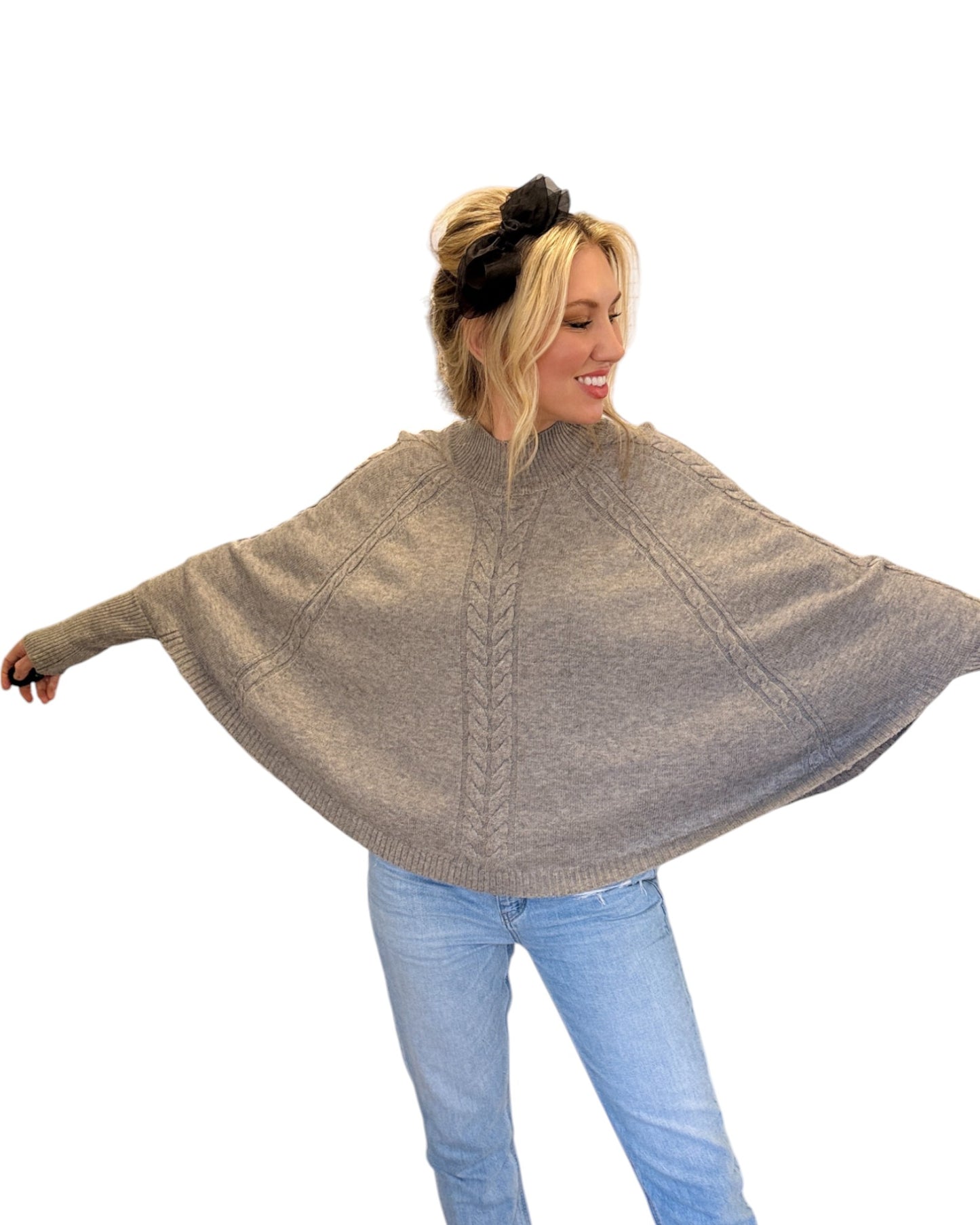 Woman wearing jeans and a Heather Grey/Taupe Cable Knit Mock Neck Poncho with a relaxed silhouette, cable knit design, and fitted sleeve hem, perfect for cozy layering.