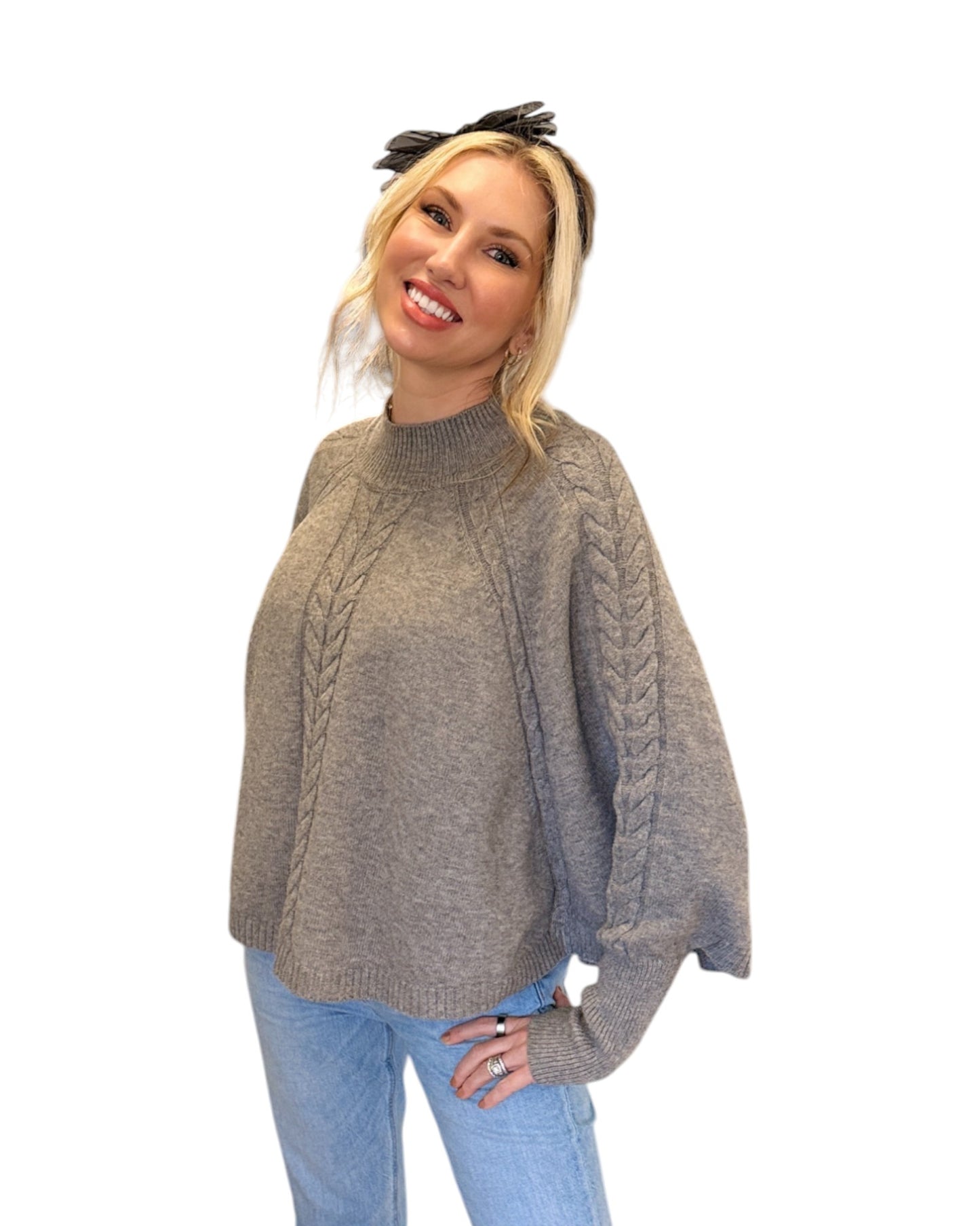 Woman wearing jeans and a Heather Grey/Taupe Cable Knit Mock Neck Poncho with a relaxed silhouette, cable knit design, and fitted sleeve hem, perfect for cozy layering.