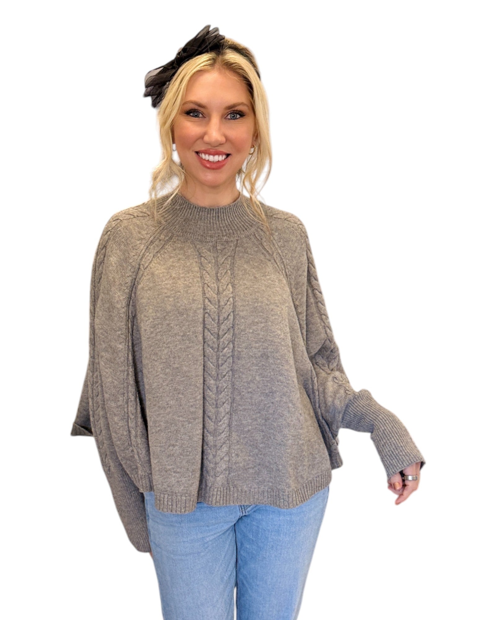 Woman wearing jeans and a Heather Grey/Taupe Cable Knit Mock Neck Poncho with a relaxed silhouette, cable knit design, and fitted sleeve hem, perfect for cozy layering.