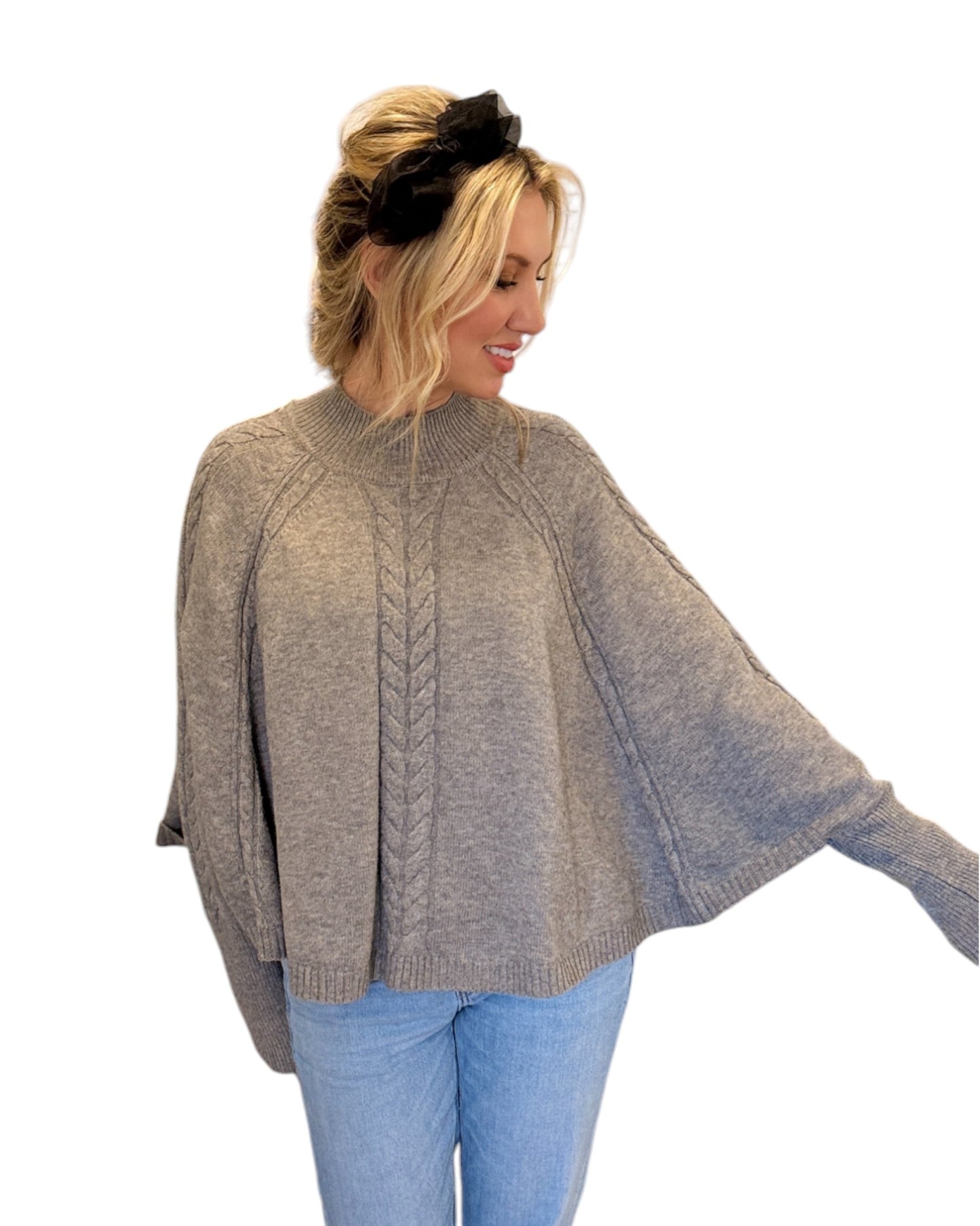 Woman wearing jeans and a Heather Grey/Taupe Cable Knit Mock Neck Poncho with a relaxed silhouette, cable knit design, and fitted sleeve hem, perfect for cozy layering.