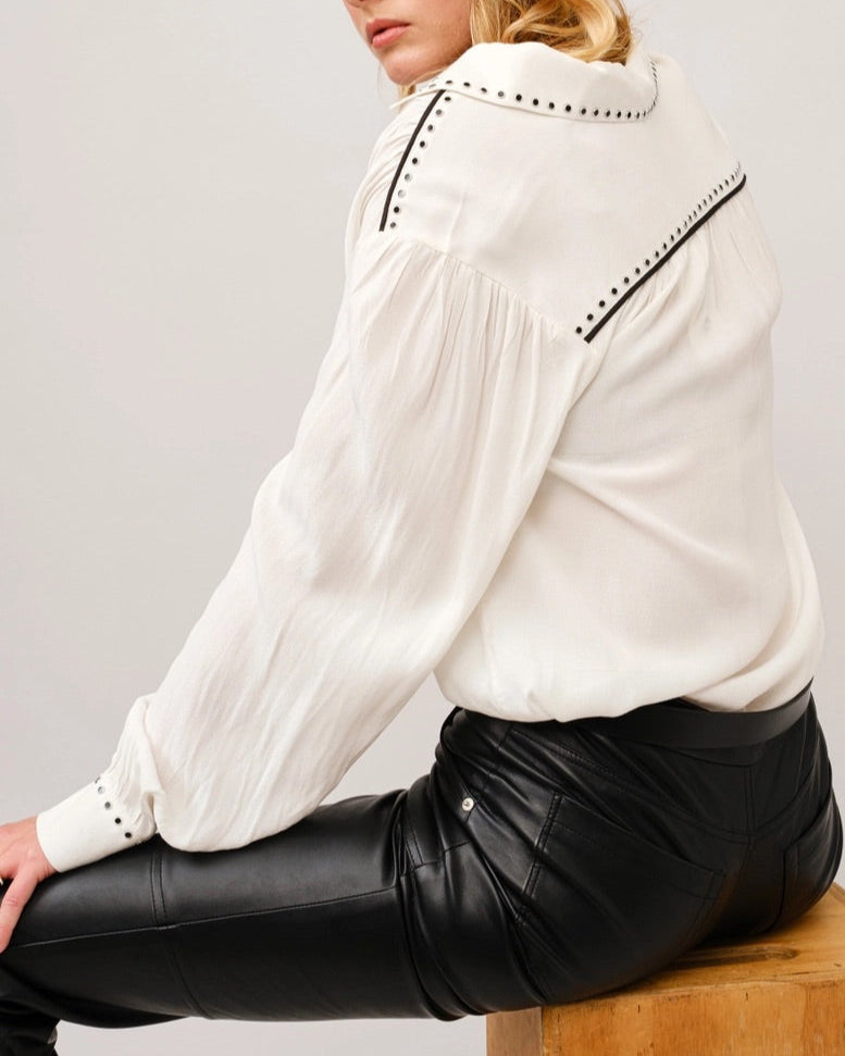 White crepe blouse with studded details, black piping on shoulders, classic collar, and slit neckline with hook closures. 