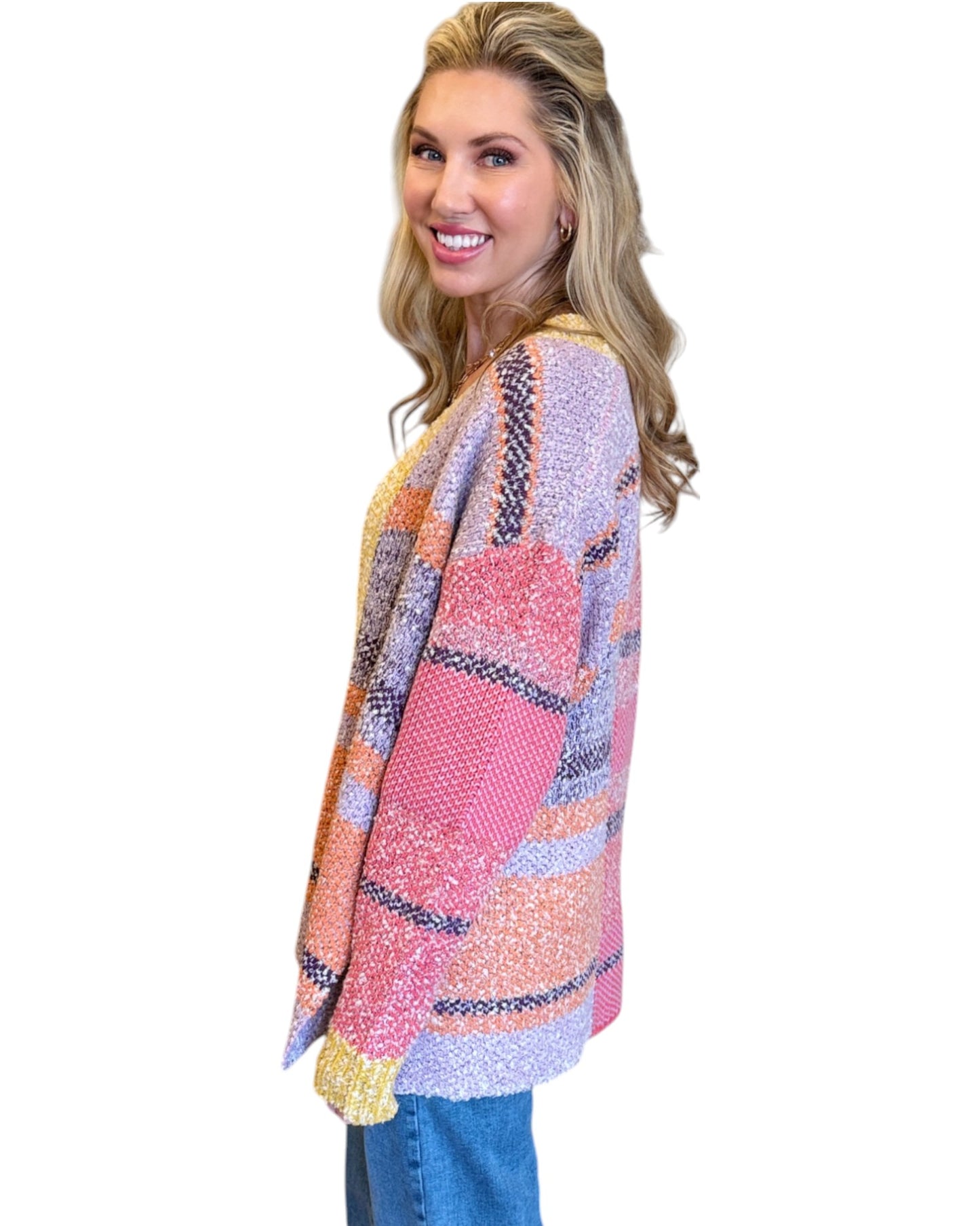 Woman wearing the Tenley Knit Dreamer Cardigan in vibrant purple, coral, and yellow tones, paired with a bright pink tank top and mid-rise wide-leg jeans. She accessorizes with a custom charm necklace made at Wish Upon Boutique, smiling against a white background.