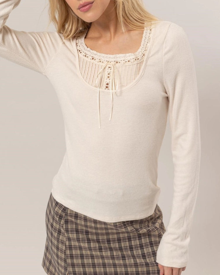 Cream ribbed knit long-sleeve top with a scoop neckline, lace trim, tie detail, and ruffled cuffs.