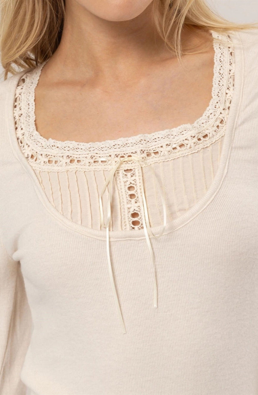 Cream ribbed knit long-sleeve top with a scoop neckline, lace trim, tie detail, and ruffled cuffs.