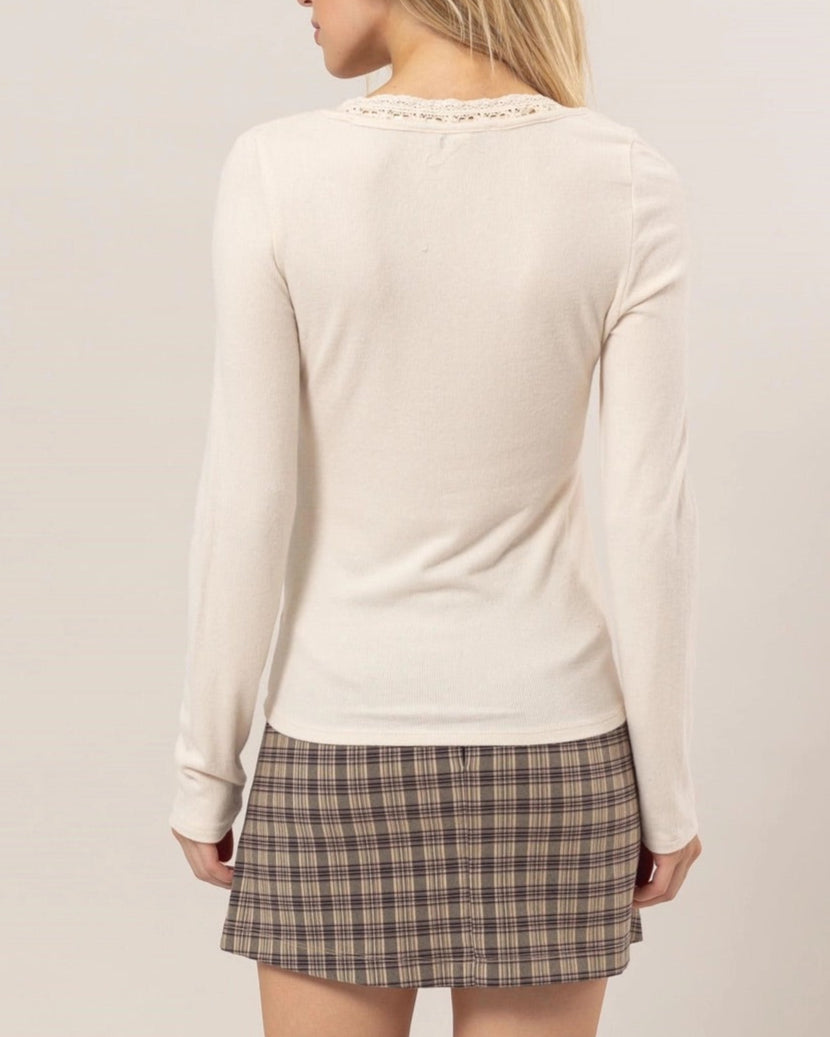 Cream ribbed knit long-sleeve top with a scoop neckline, lace trim, tie detail, and ruffled cuffs.