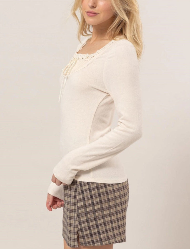 Cream ribbed knit long-sleeve top with a scoop neckline, lace trim, tie detail, and ruffled cuffs.