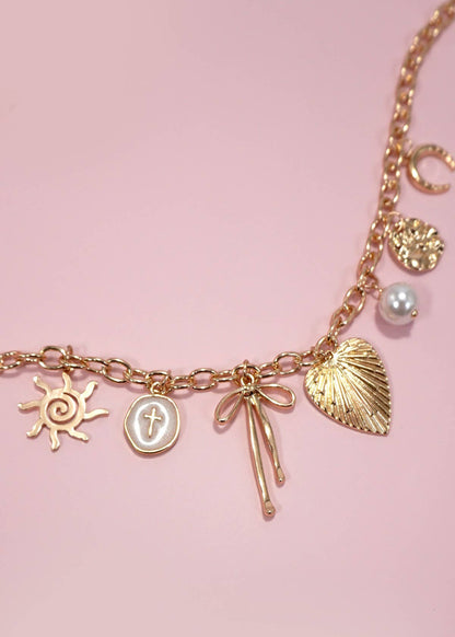 Gold statement charm necklace with a sun, cross, bow, heart, pearl and horseshoe accent. 